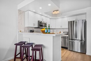 A modern kitchen with white cabinets, stainless steel appliances, and a marble backsplash. - Valley Isle Villas | Oceanfront Studio Sleeps 4 | Car Incl. w/ 6+ Nights | VIR-107 by KBM (Lahaina)