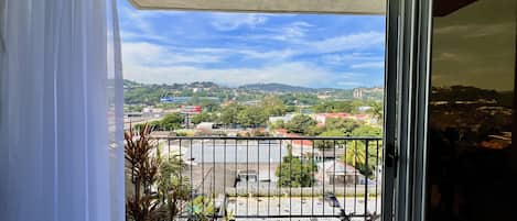 A balcony with a view of a cityscape, potted plants, and a metal railing.