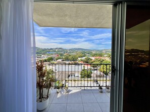 A balcony with a view of a cityscape, potted plants, and a metal railing.