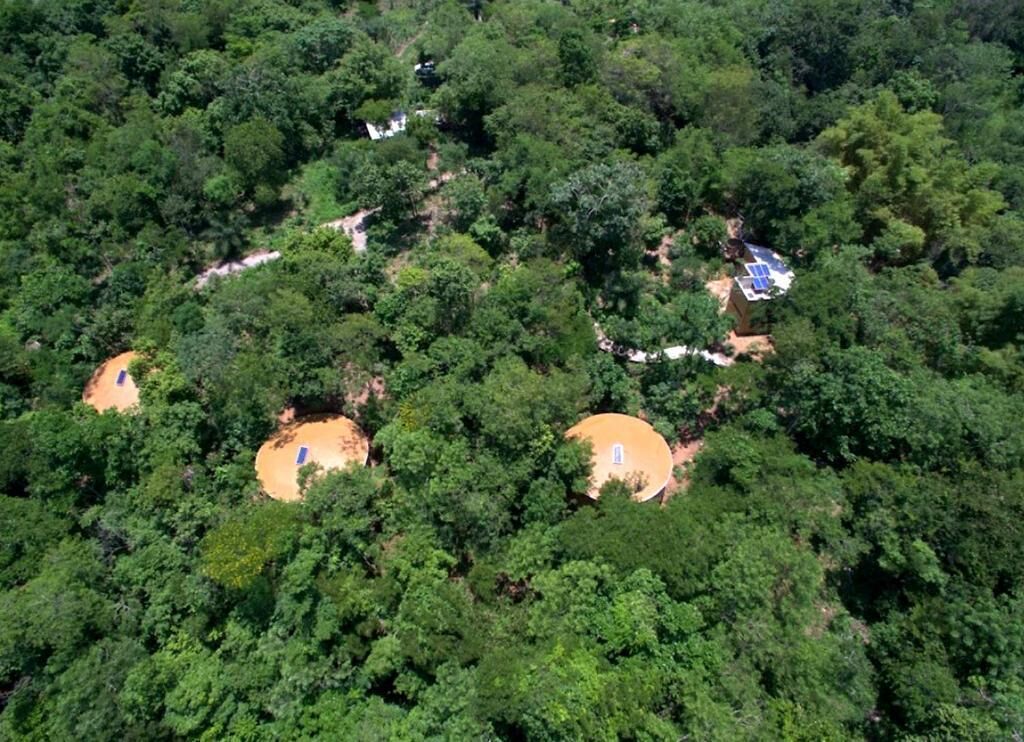 A forested area with three circular structures, possibly cabins, surrounded by dense trees.