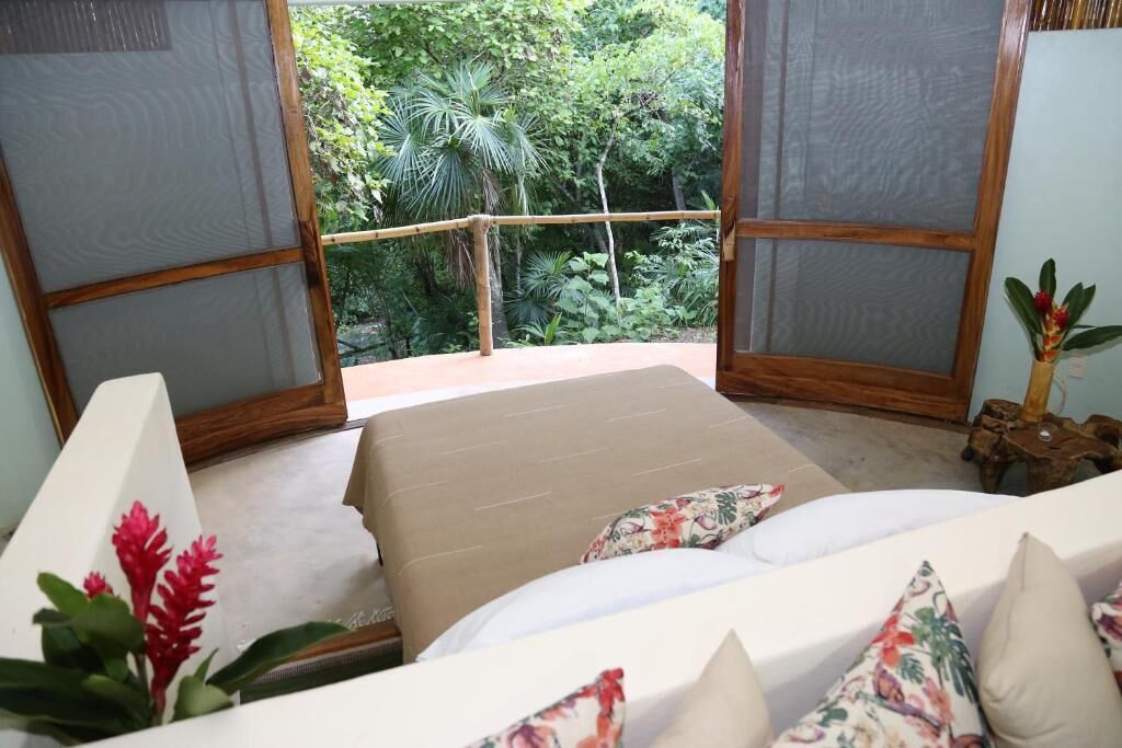 A room with a bed, a view of greenery outside, and a wooden railing.
