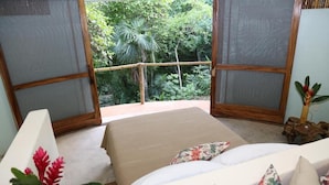 Quarto com cama, vista para o verde lá fora e corrimão de madeira.