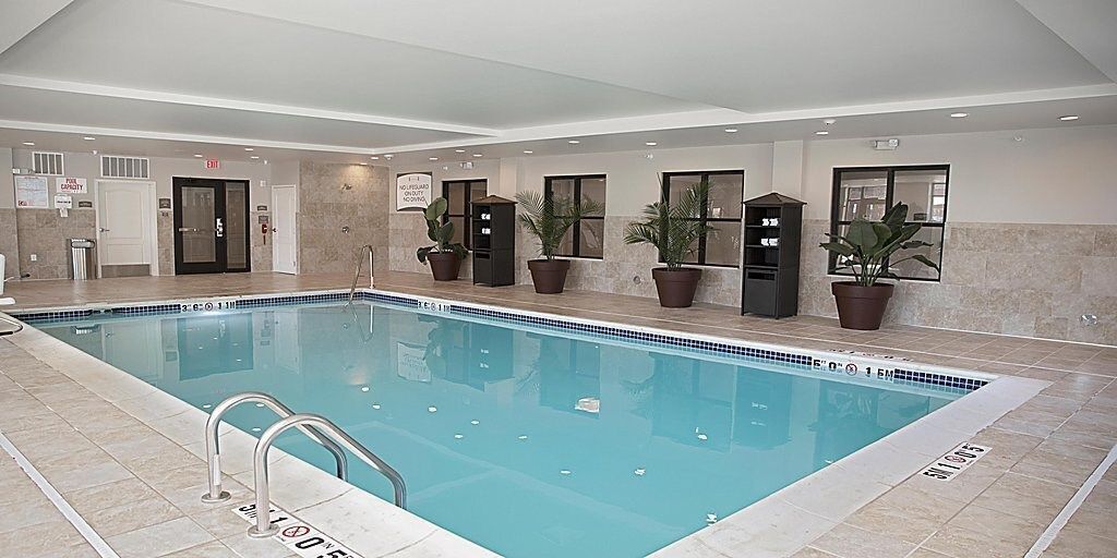 An indoor swimming pool with clear water, surrounded by potted plants and a tiled floor.