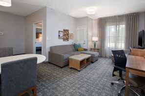 A hotel room with a bed, a sofa, a desk with a computer, a chair, and a small table.