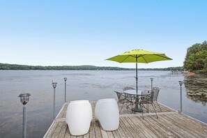 En træterrasse med et bord, stole, en grøn parasol og to hvide plantekasser.