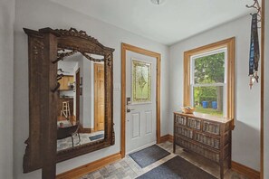 A hallway with a large mirror, a door with a stained glass window, and a window with a view of greenery.