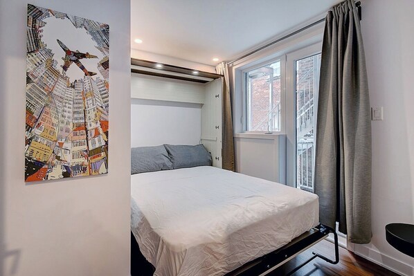 A bedroom with a bed, a window, a curtain, and a wall-mounted artwork.