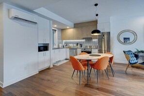 A modern kitchen with white cabinets, a stainless steel refrigerator, and a dining area with orange chairs.