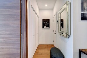 A hallway with wooden flooring, white walls, a bench, a framed mirror, and a door. - Modern 2BR Condo in Prime Montreal Location (Montreal)