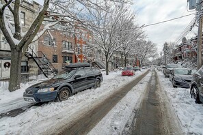 A snow-covered street with parked cars and residential buildings.