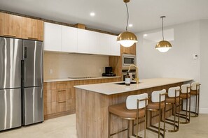 A modern kitchen with a stainless steel refrigerator, wooden cabinets, a central island with bar stools, and pendant lighting. - Massive 9BR Luxury Stay • Plateau • sleep 22 (Montréal)