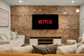 A living room with a brick wall, a flat-screen TV mounted above a wooden entertainment unit, and a modern sofa. - Massive 9BR Luxury Stay • Plateau • sleep 22 (Montréal)