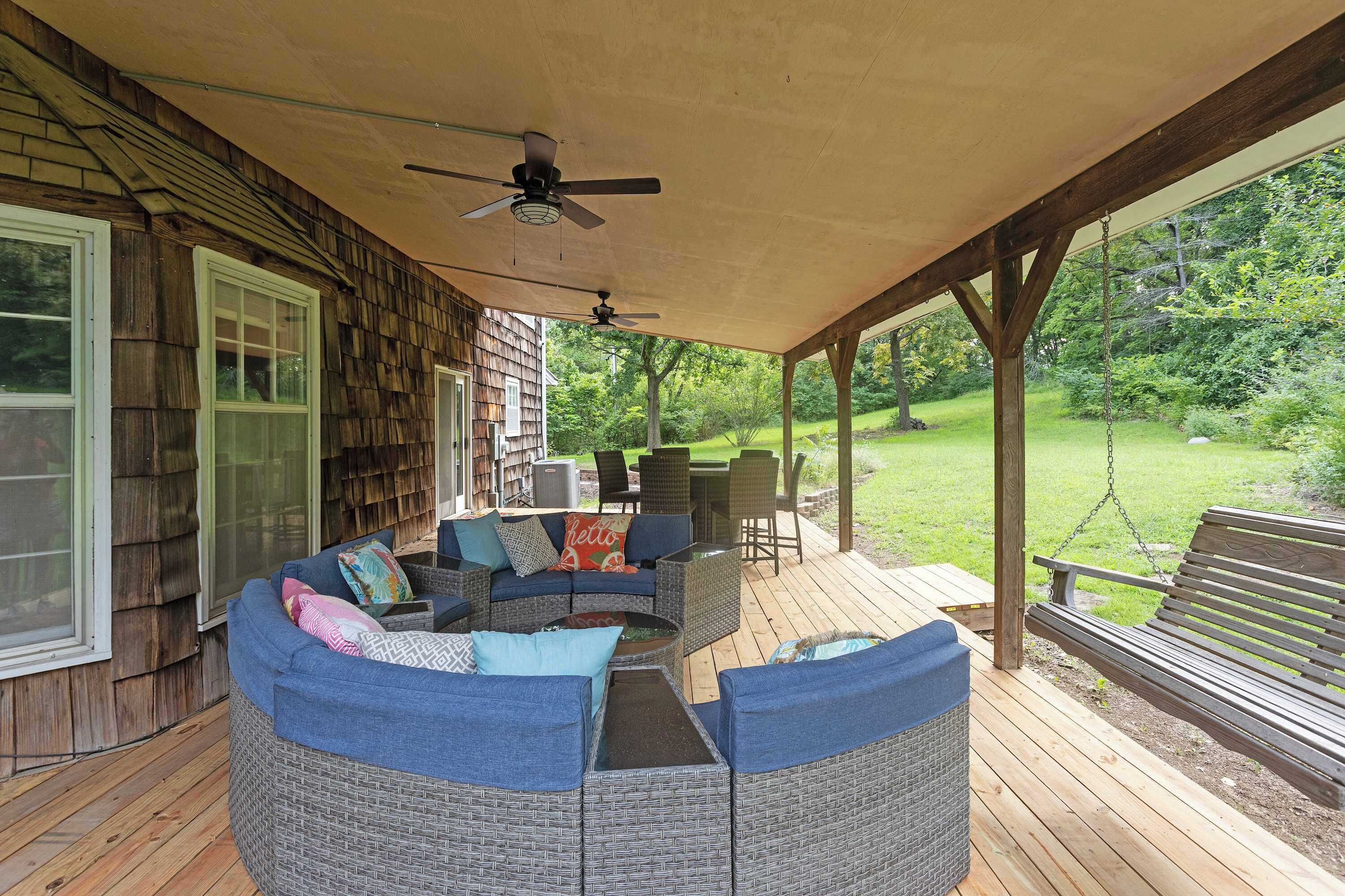 A covered outdoor seating area with a sofa and chairs, a ceiling fan, and a view of a grassy yard.