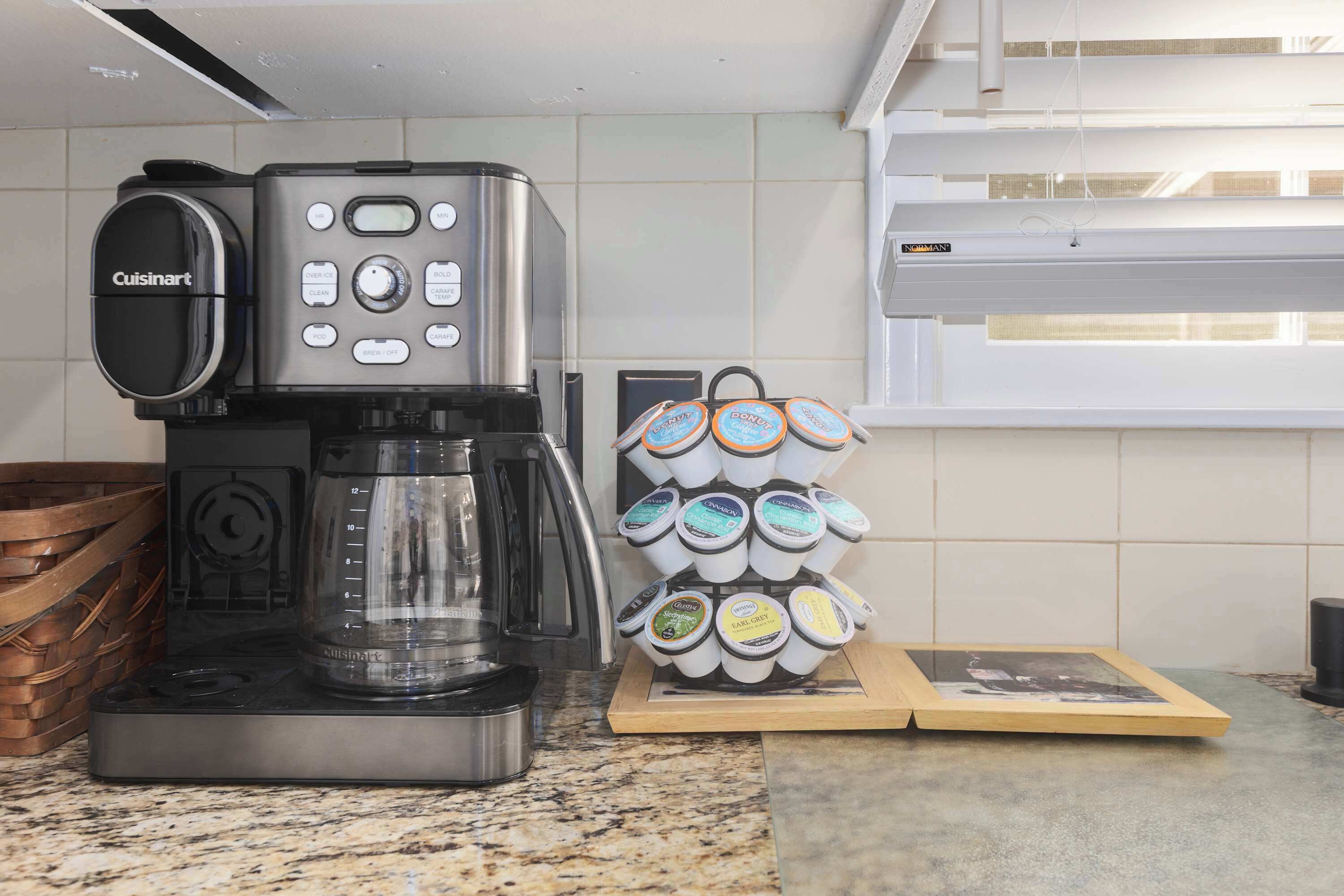 A Cuisinart espresso machine with a coffee grinder and a stack of coffee pods on a kitchen counter.