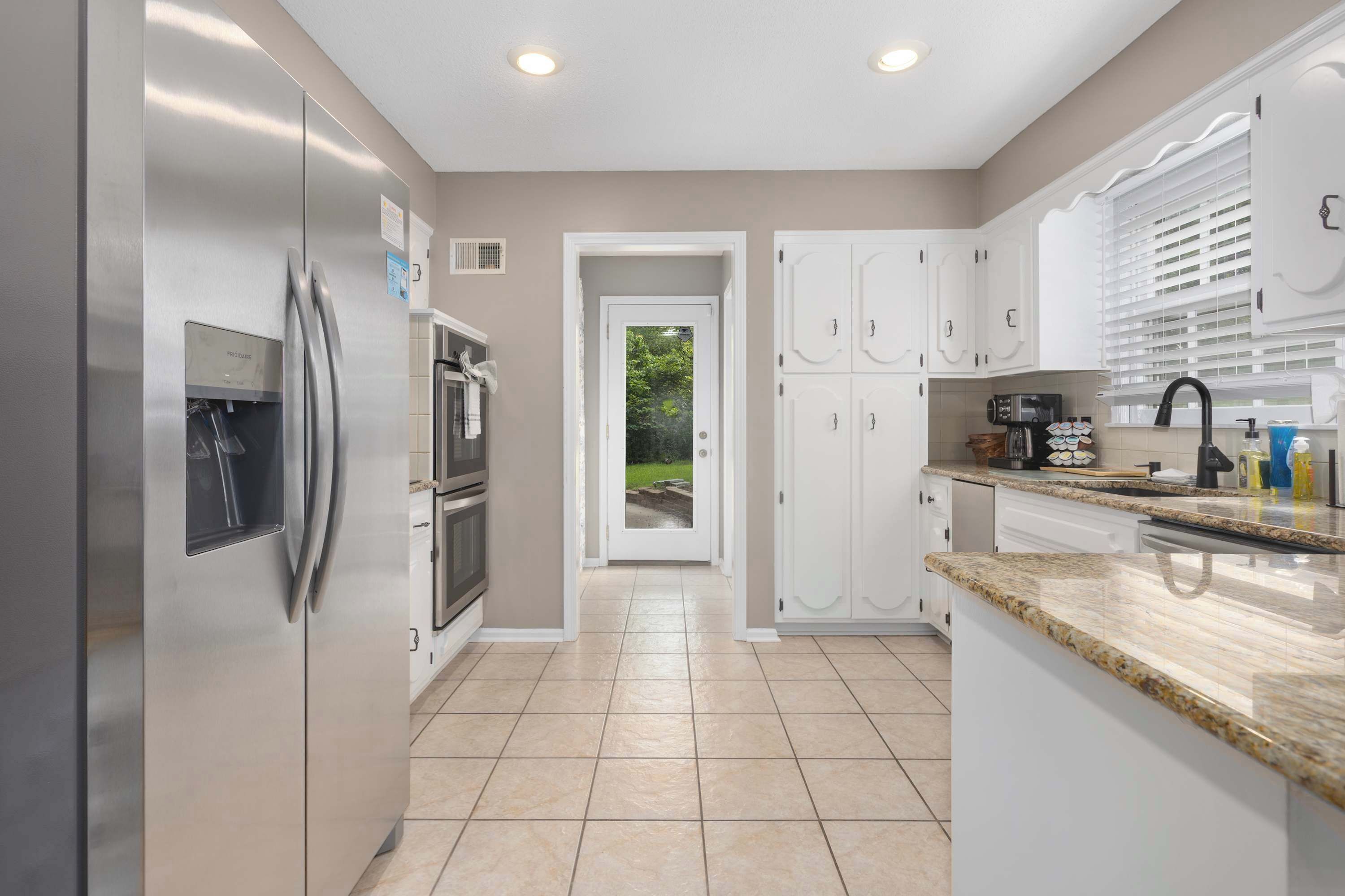 A modern kitchen with stainless steel appliances, white cabinetry, and a granite countertop.
