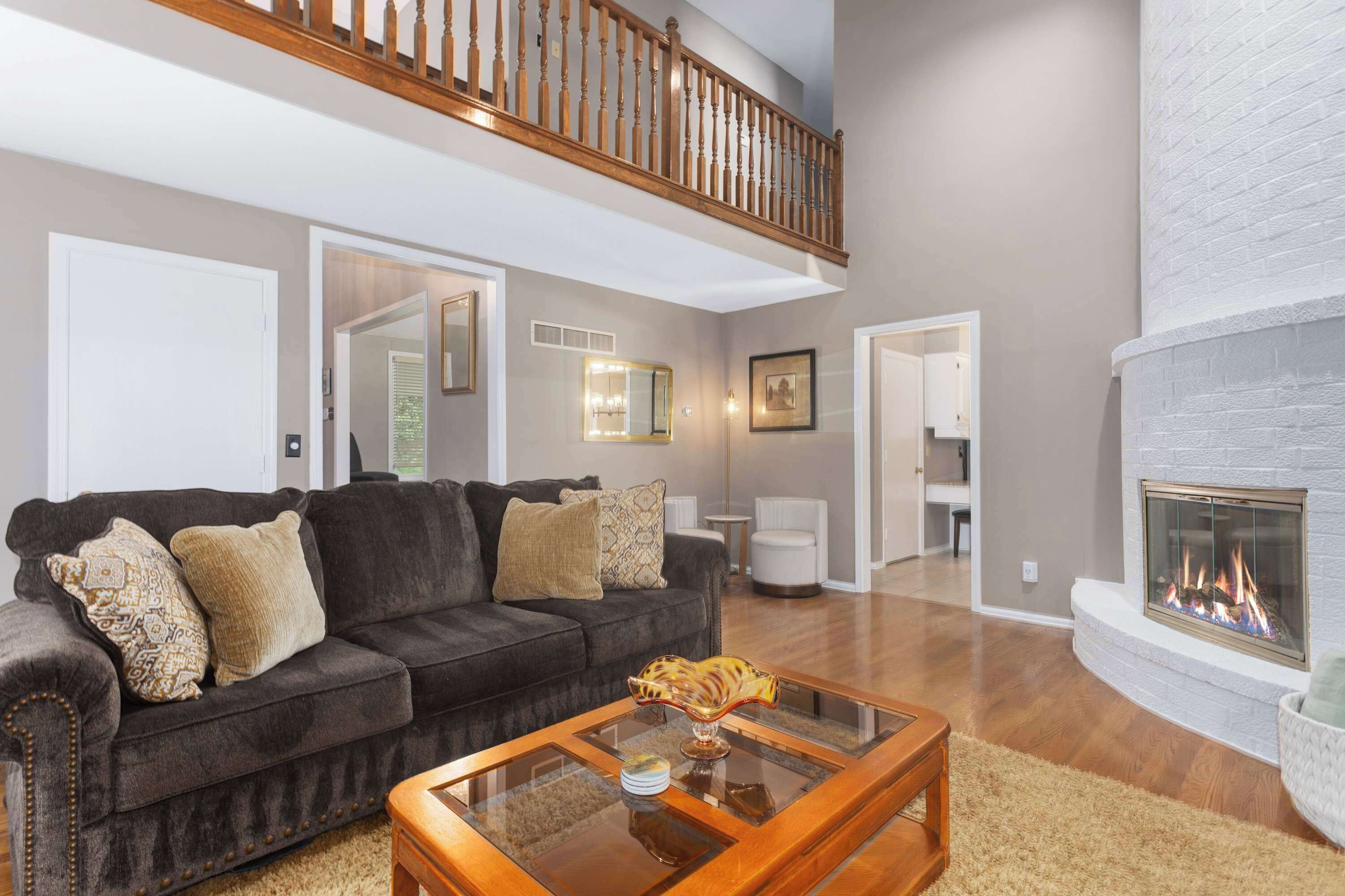 A spacious living room with a dark grey sofa, a glass coffee table, and a fireplace.
