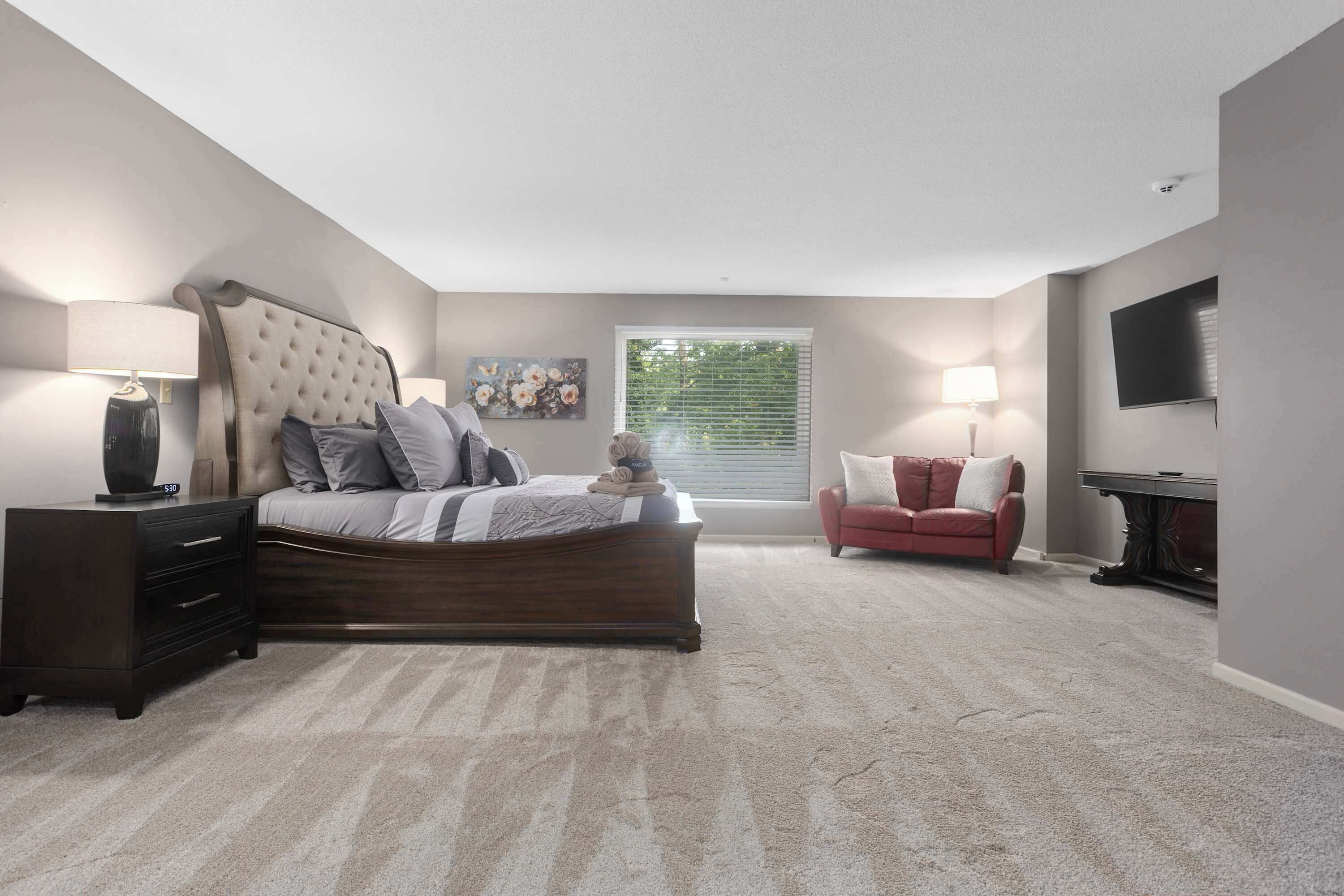 A bedroom with a bed, a nightstand, a dresser, a chair, a TV, and a window with blinds.