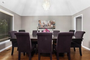 Comedor con una mesa rectangular rodeada de seis sillas, una araña colgante y un cuadro en la pared.