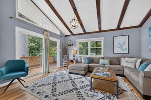 A spacious living room with a large window, a wooden ceiling, and a cozy sofa set.