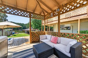 A covered outdoor patio with a cushioned seating area, a wooden deck, and a view of a backyard. - The Cove on Jackson Lake, Sleeps 9, Waterfront, Games, Hot tub + MORE! (Jackson)