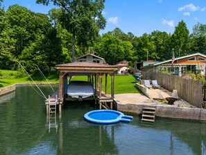 A backyard with a wooden dock, a small covered area, a blue inflatable pool, and a fenced patio with lounge chairs.