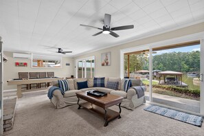 A spacious living room with a large window, a ceiling fan, and a poolside view. - The Cove on Jackson Lake, Sleeps 9, Waterfront, Games, Hot tub + MORE! (Jackson)