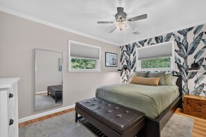 A bedroom with a bed, a bench, a ceiling fan, a mirror, and a window with a view of greenery. - The Cove on Jackson Lake, Sleeps 9, Waterfront, Games, Hot tub + MORE! (Jackson)