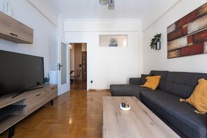Ein modernes Wohnzimmer mit Flachbildfernseher, einem dunklen Sofa, einem Holztisch und einem Bild an der Wand.