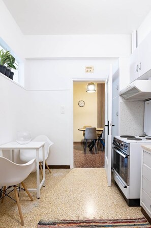 Une cuisine compacte avec des meubles blancs, une cuisinière et un coin repas comprenant des chaises et une table.