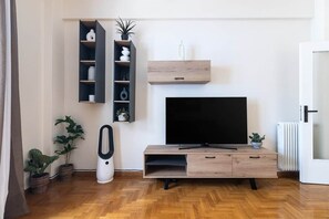 A modern living room with a flat-screen TV, wooden entertainment unit, and potted plants. - S homes | Athens · Retro-Modern 2BR · Attiki Metro (Athens)
