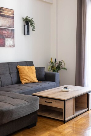 A modern living room with a grey sofa, a wooden coffee table, and a potted plant. - S homes | Athens · Retro-Modern 2BR · Attiki Metro (Athens)