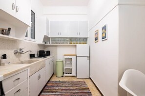 Eine kleine Küche mit weißen Schränken, einer Spüle, einem Kühlschrank und einem Mülleimer.