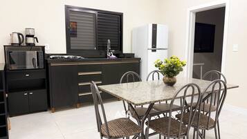 Eine kleine Küche mit Mikrowelle, Kaffeemaschine und Kühlschrank. Ein Esstisch mit Stühlen und eine Vase mit Blumen sind ebenfalls vorhanden.