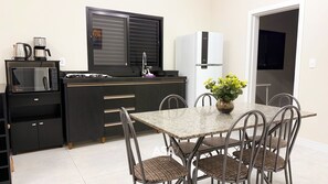 Une cuisine compacte équipée d’un four à micro-ondes, d’une machine à café et d’un réfrigérateur. On y trouve une table à manger avec des chaises et un vase rempli de fleurs.