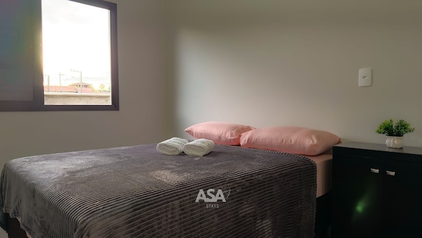 Una camera da letto con un letto, cuscini, una piccola pianta in vaso e una finestra con vista.