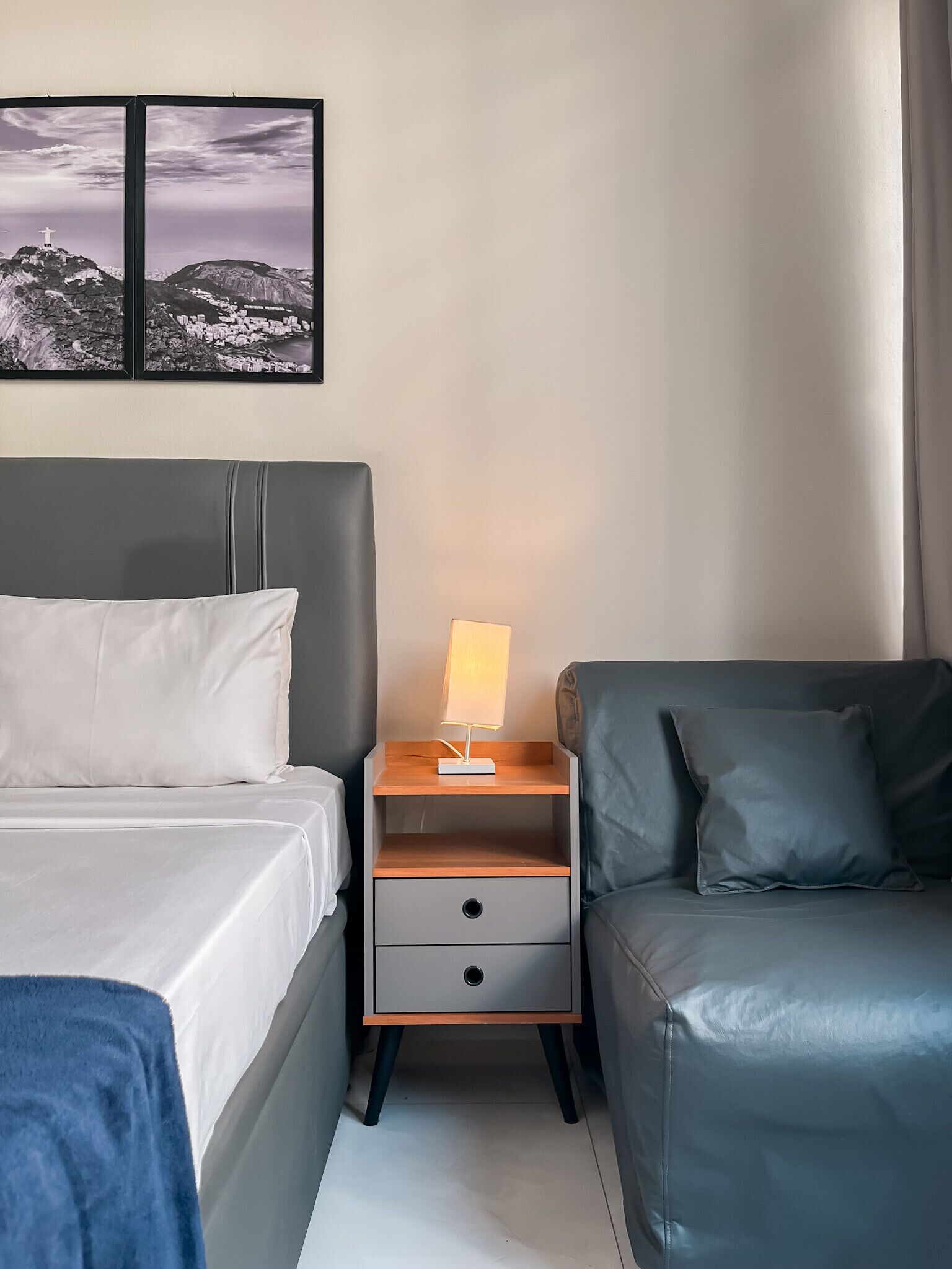 A hotel room with a bed, a nightstand with a lamp, a sofa, and a wall-mounted picture.