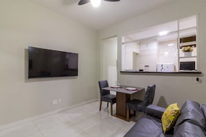 A modern living room with a flat-screen TV mounted on the wall, a dining area with a table and chairs, and a sofa with a decorative pillow. - 5 min from Copacabana Beach - B501 (Rio de Janeiro)