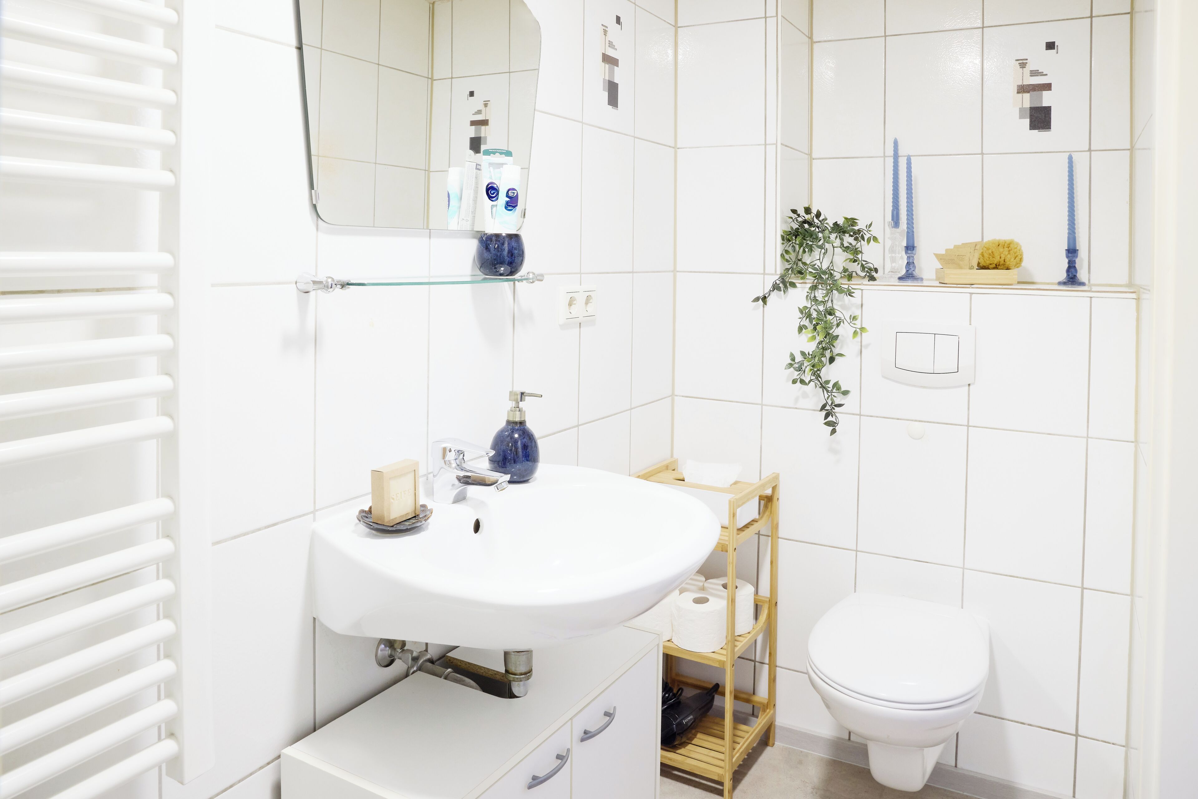 Ein Badezimmer mit einem weißen Waschbecken, einem Spiegel, einer Toilette und einem Ablagebereich mit Toilettenartikeln.