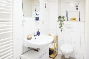 Un bagno con un lavandino bianco, uno specchio, un WC e uno scaffale con articoli da toilette.