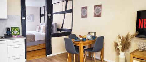 A cozy room with a bed, a desk, a dining table with chairs, and a TV on the wall.