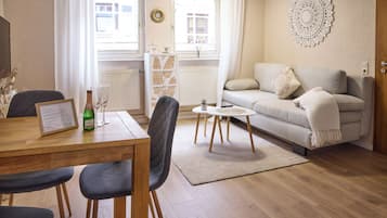 Ett möblerat vardagsrum med en soffa, ett matbord med stolar, ett litet soffbord och en dekorativ väggdekoration.