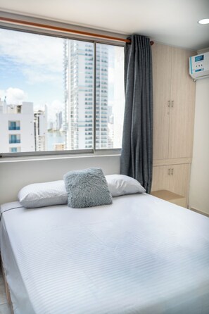 Ein Hotelzimmer mit Bett, einem Fenster mit Blick auf hohe Gebäude und einem Holzschrank.