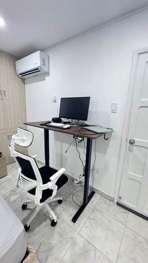 Ein Zimmer mit Schreibtisch, Computer, Stuhl und Klimaanlage.