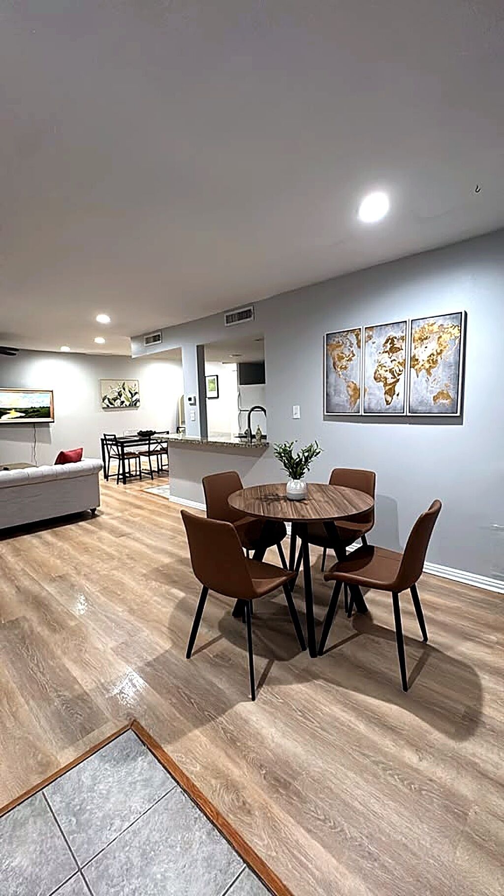 Un espace repas moderne avec une table ronde et six chaises, un canapé et une cuisine en arrière-plan.