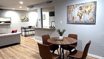 Un espace repas moderne avec une table ronde et six chaises, un canapé et une cuisine en arrière-plan.
