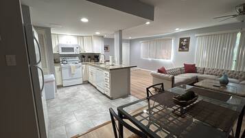 A modern kitchen with white cabinets, a stove, and a microwave. There is a dining area with a glass table and chairs.