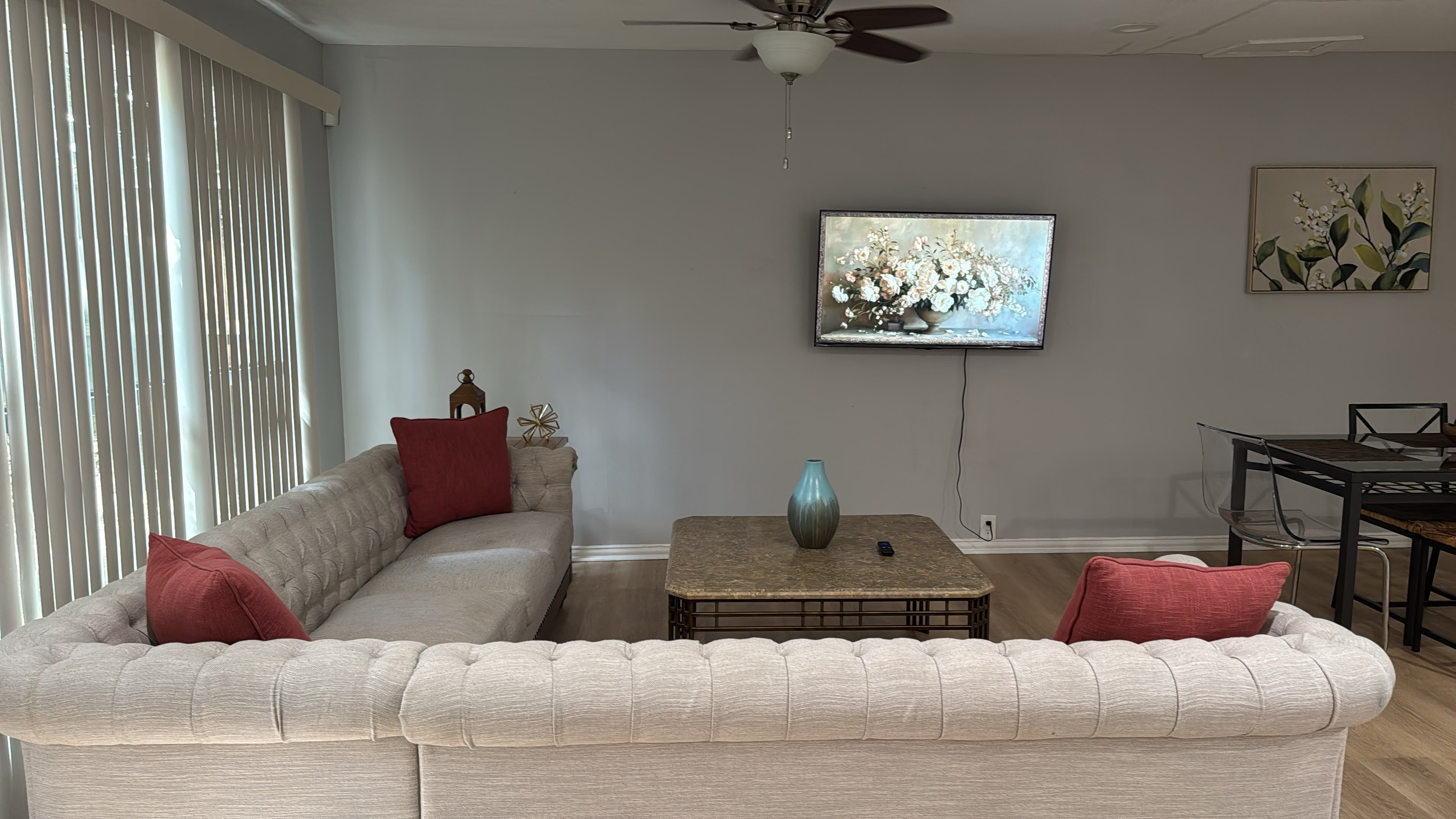 A living room with a sectional sofa, a coffee table, a TV mounted on the wall, and a dining area with a table and chairs.