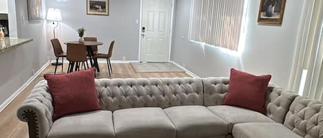 A living room with a sectional sofa, a coffee table, and a dining area in the background.