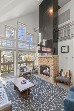 A living room with a stone fireplace, large windows, and a clock on the wall. - Ski In/Out Sunset Luxury: Etta Place Too 115 at the base of Lift 7 (Telluride)