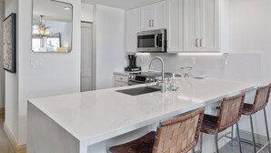 A modern kitchen with white cabinetry, a stainless steel microwave, a sink, and a bar area with two stools. - Ski In/Out Sunset Luxury: Etta Place Too 115 at the base of Lift 7 (Telluride)